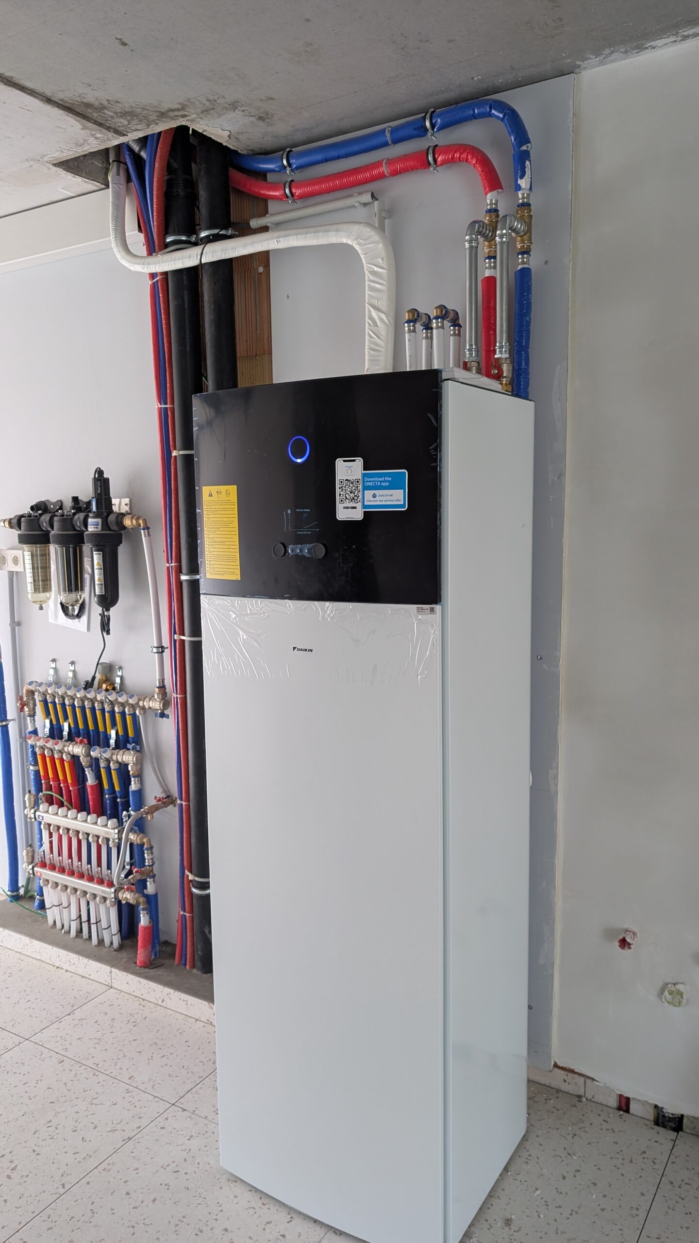 HVAC boiler with blue and red insulated pipes, water manifold, and filtration system in a utility room.